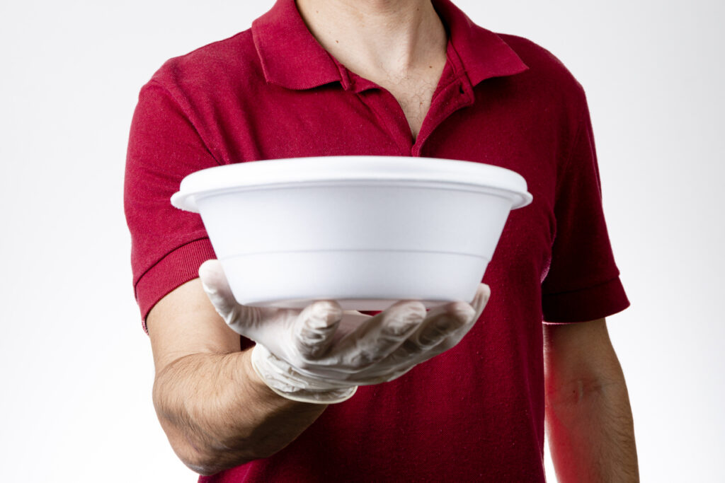 Homem utilizando luvas descartáveis segura uma marmitex. Um produto descartável essencial para cozinhas empresariais.