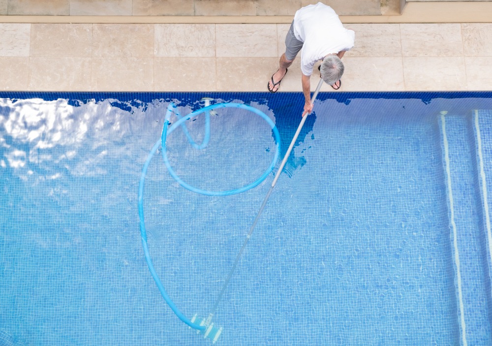 Profissional limpando piscina, uma prática ainda mais frequente durante o verão nos condomínios.