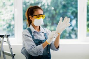 mulher de macacão usando óculos de proteção, luvas e máscara.